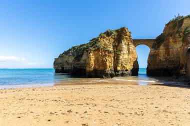 Kumsaldaki sarı kayalar ve uçurumlar. Eski Pinhao Fort Köprüsü 'nün iki uçurumu birleştirdiği deniz kenarında bir koy. Praia da Caldeira plajı, Lagos. Algarve, Portekiz
