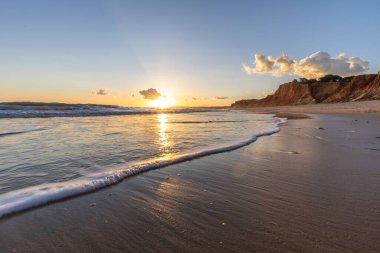 Kızıl kayalıkları ve kayalıkları olan güzel kumlu bir sahil. Günbatımında Praia do Poo Velho, Praia da Falsia, Algarve, Portekiz 'de Atlantik kıyısında sığ dalgalarla birlikte