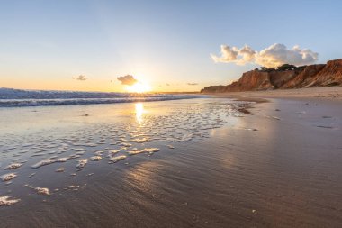 Kızıl kayalıkları ve kayalıkları olan güzel kumlu bir sahil. Gün batımında Praia do Poo Velho, Praia da Falsia, Algarve, Portekiz 'deki Atlantik kıyısının sığ ve sakin sularında yansımalar görülecek.