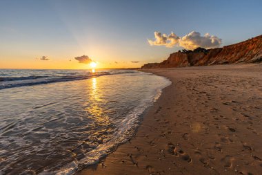 Kızıl kayalıkları ve kayalıkları olan güzel kumlu bir sahil. Gün batımında Praia do Poo Velho, Praia da Falsia, Algarve, Portekiz 'deki Atlantik kıyısının sığ ve sakin sularında yansımalar görülecek.
