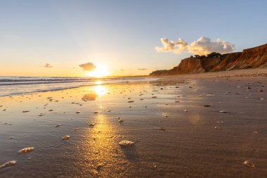 Kızıl kayalıkları ve kayalıkları olan güzel kumlu bir sahil. Gün batımında Praia do Poo Velho, Praia da Falsia, Algarve, Portekiz 'deki Atlantik kıyısının sığ ve sakin sularında yansımalar görülecek.