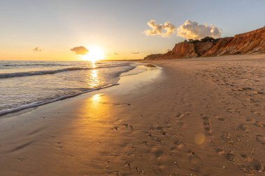 Kızıl kayalıkları ve kayalıkları olan güzel kumlu bir sahil. Günbatımında Praia do Poo Velho, Praia da Falsia, Algarve, Portekiz 'de Atlantik kıyısında sığ dalgalarla birlikte