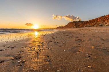 Kızıl kayalıkları ve kayalıkları olan güzel kumlu bir sahil. Günbatımında Praia do Poo Velho, Praia da Falsia, Algarve, Portekiz 'de Atlantik kıyısında sığ dalgalarla birlikte