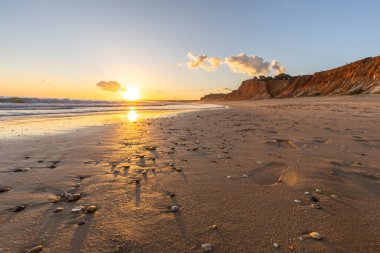Kızıl kayalıkları ve kayalıkları olan güzel kumlu bir sahil. Günbatımında Praia do Poo Velho, Praia da Falsia, Algarve, Portekiz 'de Atlantik kıyısında sığ dalgalarla birlikte