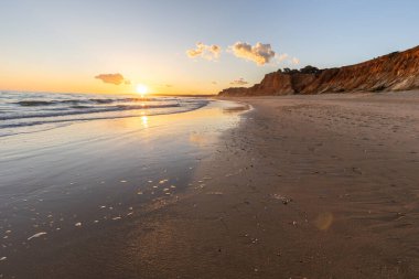 Kızıl kayalıkları ve kayalıkları olan güzel kumlu bir sahil. Gün batımında Praia do Poo Velho, Praia da Falsia, Algarve, Portekiz 'deki Atlantik kıyısının sığ ve sakin sularında yansımalar görülecek.