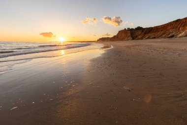 Kızıl kayalıkları ve kayalıkları olan güzel kumlu bir sahil. Günbatımında Praia do Poo Velho, Praia da Falsia, Algarve, Portekiz 'de Atlantik kıyısında sığ dalgalarla birlikte