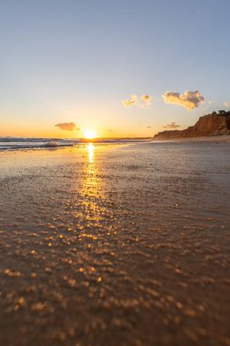 Kızıl kayalıkları ve kayalıkları olan güzel kumlu bir sahil. Gün batımında Praia do Poo Velho, Praia da Falsia, Algarve, Portekiz 'deki Atlantik kıyısının sığ ve sakin sularında yansımalar görülecek.