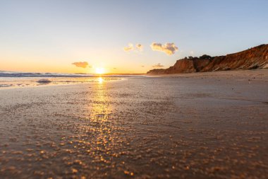 Kızıl kayalıkları ve kayalıkları olan güzel kumlu bir sahil. Gün batımında Praia do Poo Velho, Praia da Falsia, Algarve, Portekiz 'deki Atlantik kıyısının sığ ve sakin sularında yansımalar görülecek.