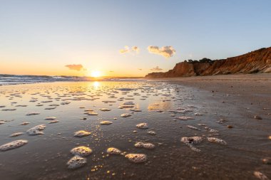 Kızıl kayalıkları ve kayalıkları olan güzel kumlu bir sahil. Gün batımında Praia do Poo Velho, Praia da Falsia, Algarve, Portekiz 'deki Atlantik kıyısının sığ ve sakin sularında yansımalar görülecek.