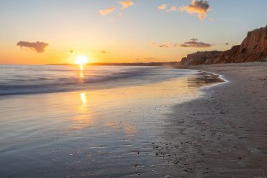Kızıl kayalıkları ve kayalıkları olan güzel kumlu bir sahil. Gün batımında Praia do Poo Velho, Praia da Falsia, Algarve, Portekiz 'deki Atlantik kıyısının sığ ve sakin sularında yansımalar görülecek.