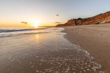 Kızıl kayalıkları ve kayalıkları olan güzel kumlu bir sahil. Gün batımında Praia do Poo Velho, Praia da Falsia, Algarve, Portekiz 'deki Atlantik kıyısının sığ ve sakin sularında yansımalar görülecek.