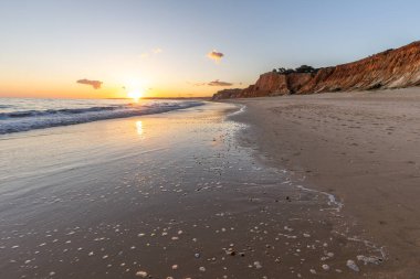Kızıl kayalıkları ve kayalıkları olan güzel kumlu bir sahil. Gün batımında Praia do Poo Velho, Praia da Falsia, Algarve, Portekiz 'deki Atlantik kıyısının sığ ve sakin sularında yansımalar görülecek.