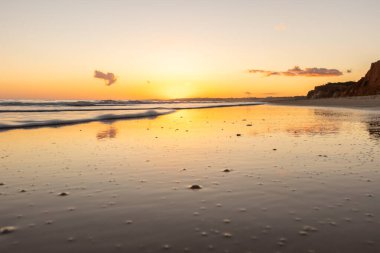 Kızıl kayalıkları ve kayalıkları olan güzel kumlu bir sahil. Gün batımında Praia do Poo Velho, Praia da Falsia, Algarve, Portekiz 'deki Atlantik kıyısının sığ ve sakin sularında yansımalar görülecek.