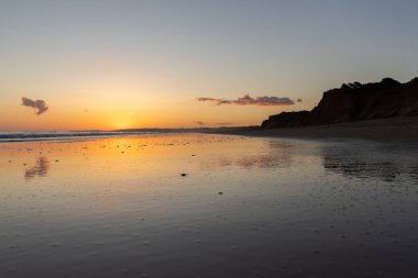 Kızıl kayalıkları ve kayalıkları olan güzel kumlu bir sahil. Gün batımında Praia do Poo Velho, Praia da Falsia, Algarve, Portekiz 'deki Atlantik kıyısının sığ ve sakin sularında yansımalar görülecek.