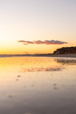 Kızıl kayalıkları ve kayalıkları olan güzel kumlu bir sahil. Gün batımında Praia do Poo Velho, Praia da Falsia, Algarve, Portekiz 'deki Atlantik kıyısının sığ ve sakin sularında yansımalar görülecek.