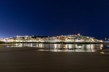 Kumlu bir sahil ve alçak gelgitte limanın gece görüntüsü. Şafakta Ferragudo, Portimo, Algarve, Portekiz 'de aydınlatılmış tarihi bir kasabanın panoramik görüntüsü