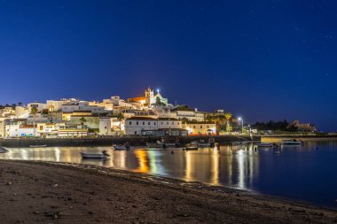 Kumlu bir sahil ve alçak gelgitte limanın gece görüntüsü. Şafakta Ferragudo, Portimo, Algarve, Portekiz 'de aydınlatılmış tarihi bir kasabanın panoramik görüntüsü