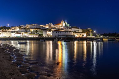 Kumlu bir sahil ve alçak gelgitte limanın gece görüntüsü. Şafakta Ferragudo, Portimo, Algarve, Portekiz 'de aydınlatılmış tarihi bir kasabanın panoramik görüntüsü
