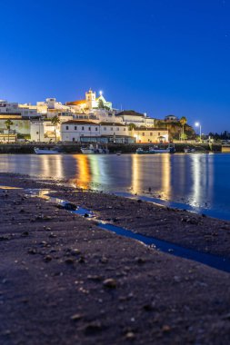 Kumlu bir sahil ve alçak gelgitte limanın gece görüntüsü. Şafakta Ferragudo, Portimo, Algarve, Portekiz 'de aydınlatılmış tarihi bir kasabanın panoramik görüntüsü