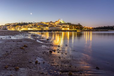 Kumlu bir sahil ve alçak gelgitte limanın gece görüntüsü. Şafakta Ferragudo, Portimo, Algarve, Portekiz 'de aydınlatılmış tarihi bir kasabanın panoramik görüntüsü