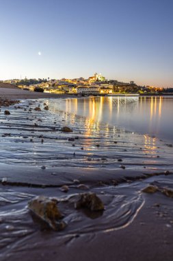 Kumlu bir sahil ve alçak gelgitte limanın gece görüntüsü. Şafakta Ferragudo, Portimo, Algarve, Portekiz 'de aydınlatılmış tarihi bir kasabanın panoramik görüntüsü