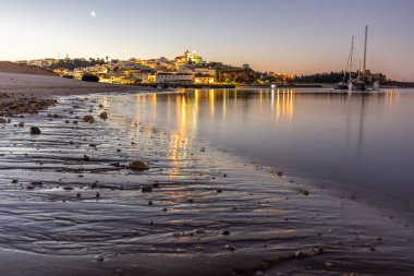 Kumlu bir sahil ve alçak gelgitte limanın gece görüntüsü. Şafakta Ferragudo, Portimo, Algarve, Portekiz 'de aydınlatılmış tarihi bir kasabanın panoramik görüntüsü
