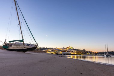 Kumlu bir sahil ve alçak gelgitte limanın gece görüntüsü. Şafakta Ferragudo, Portimo, Algarve, Portekiz 'de aydınlatılmış tarihi bir kasabanın panoramik görüntüsü