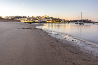 Kumlu bir sahil ve alçak gelgitte limanın gece görüntüsü. Şafakta Ferragudo, Portimo, Algarve, Portekiz 'de aydınlatılmış tarihi bir kasabanın panoramik görüntüsü