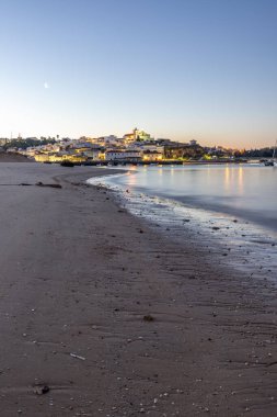 Kumlu bir sahil ve alçak gelgitte limanın gece görüntüsü. Şafakta Ferragudo, Portimo, Algarve, Portekiz 'de aydınlatılmış tarihi bir kasabanın panoramik görüntüsü
