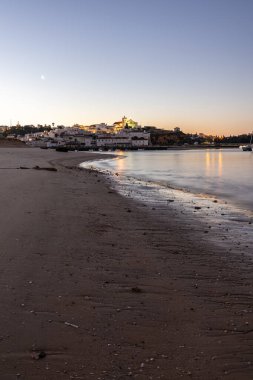 Kumlu bir sahil ve alçak gelgitte limanın gece görüntüsü. Şafakta Ferragudo, Portimo, Algarve, Portekiz 'de aydınlatılmış tarihi bir kasabanın panoramik görüntüsü