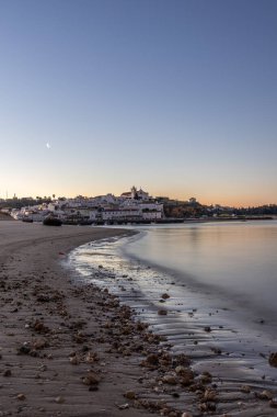 Kumlu bir sahil ve alçak gelgitte limanın gece görüntüsü. Şafakta Ferragudo, Portimo, Algarve, Portekiz 'de aydınlatılmış tarihi bir kasabanın panoramik görüntüsü
