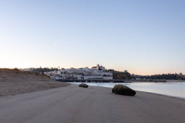 Kumlu bir sahil ve alçak gelgitte limanın gece görüntüsü. Şafakta Ferragudo, Portimo, Algarve, Portekiz 'de aydınlatılmış tarihi bir kasabanın panoramik görüntüsü