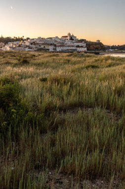 Güneşin doğuşu çayıra, kumlu plaja ve alçak gelgitte limana bakıyor. Sabahın köründe Ferragudo, Portimo, Algarve, Portekiz 'de tarihi bir kasabanın panoramik görüntüsü.