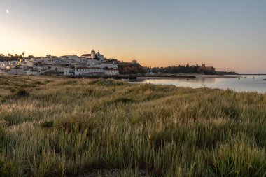 Güneşin doğuşu çayıra, kumlu plaja ve alçak gelgitte limana bakıyor. Sabahın köründe Ferragudo, Portimo, Algarve, Portekiz 'de tarihi bir kasabanın panoramik görüntüsü.