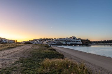 Güneşin doğuşu çayıra, kumlu plaja ve alçak gelgitte limana bakıyor. Sabahın köründe Ferragudo, Portimo, Algarve, Portekiz 'de tarihi bir kasabanın panoramik görüntüsü.