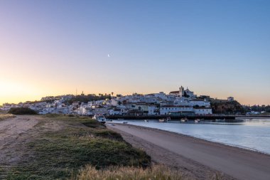 Güneşin doğuşu çayıra, kumlu plaja ve alçak gelgitte limana bakıyor. Sabahın köründe Ferragudo, Portimo, Algarve, Portekiz 'de tarihi bir kasabanın panoramik görüntüsü.