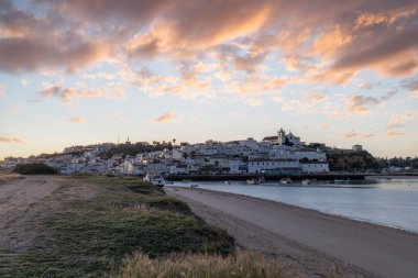Güneşin doğuşu çayıra, kumlu plaja ve alçak gelgitte limana bakıyor. Sabahın köründe Ferragudo, Portimo, Algarve, Portekiz 'de tarihi bir kasabanın panoramik görüntüsü.