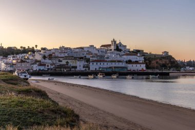 Güneşin doğuşu çayıra, kumlu plaja ve alçak gelgitte limana bakıyor. Sabahın köründe Ferragudo, Portimo, Algarve, Portekiz 'de tarihi bir kasabanın panoramik görüntüsü.