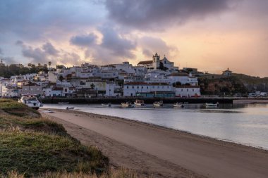 Güneşin doğuşu çayıra, kumlu plaja ve alçak gelgitte limana bakıyor. Sabahın köründe Ferragudo, Portimo, Algarve, Portekiz 'de tarihi bir kasabanın panoramik görüntüsü.