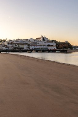 Kumsala bakan bir gün doğumu ve alçak gelgitte liman. Günbatımında Ferragudo, Portimo, Algarve, Portekiz 'de tarihi bir kasabanın panoramik manzarası