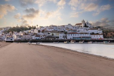 Kumsala bakan bir gün doğumu ve alçak gelgitte liman. Günbatımında Ferragudo, Portimo, Algarve, Portekiz 'de tarihi bir kasabanın panoramik manzarası