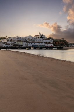 Kumsala bakan bir gün doğumu ve alçak gelgitte liman. Günbatımında Ferragudo, Portimo, Algarve, Portekiz 'de tarihi bir kasabanın panoramik manzarası