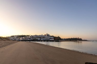 Kumsala bakan bir gün doğumu ve alçak gelgitte liman. Günbatımında Ferragudo, Portimo, Algarve, Portekiz 'de tarihi bir kasabanın panoramik manzarası