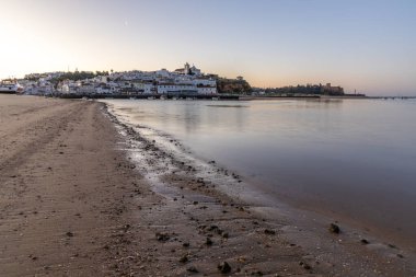 Kumsala bakan bir gün doğumu ve alçak gelgitte liman. Günbatımında Ferragudo, Portimo, Algarve, Portekiz 'de tarihi bir kasabanın panoramik manzarası
