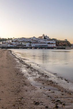 Kumsala bakan bir gün doğumu ve alçak gelgitte liman. Günbatımında Ferragudo, Portimo, Algarve, Portekiz 'de tarihi bir kasabanın panoramik manzarası