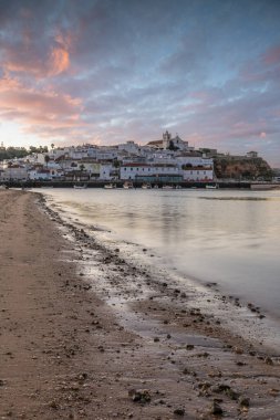 Kumsala bakan bir gün doğumu ve alçak gelgitte liman. Günbatımında Ferragudo, Portimo, Algarve, Portekiz 'de tarihi bir kasabanın panoramik manzarası