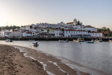 Kumsala bakan bir gün doğumu ve alçak gelgitte liman. Günbatımında Ferragudo, Portimo, Algarve, Portekiz 'de tarihi bir kasabanın panoramik manzarası