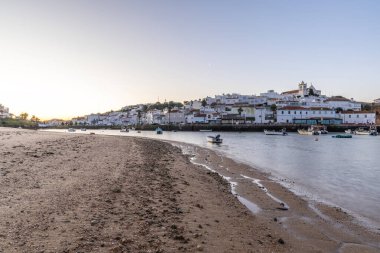 Kumsala bakan bir gün doğumu ve alçak gelgitte liman. Günbatımında Ferragudo, Portimo, Algarve, Portekiz 'de tarihi bir kasabanın panoramik manzarası
