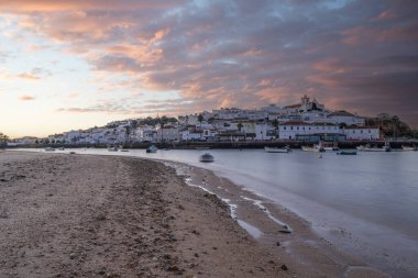 Kumsala bakan bir gün doğumu ve alçak gelgitte liman. Günbatımında Ferragudo, Portimo, Algarve, Portekiz 'de tarihi bir kasabanın panoramik manzarası