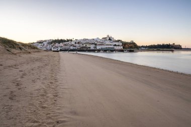 Kumsala bakan bir gün doğumu ve alçak gelgitte liman. Günbatımında Ferragudo, Portimo, Algarve, Portekiz 'de tarihi bir kasabanın panoramik manzarası